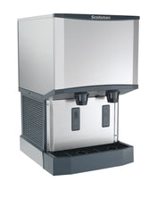 A sleek, industrial stainless steel ice and water dispenser offers nugget ice and water with two push levers labeled “ICE” and “WATER,” plus a black drip tray and side ventilation grates for efficient touchfree dispensing.