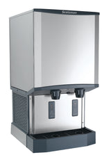 A stainless steel Scotsman ice and water dispenser with touchfree infrared dispensing, two digital displays, and a drip tray at the base. The sleek, boxy nugget ice machine is designed for countertop or freestanding use.