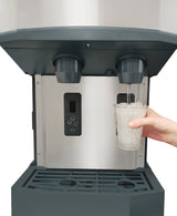 A hand holds a clear plastic cup filled with ice under a Scotsman HID540A-1 ice and water dispenser. Water flows from the right spout, while the left is idle. The commercial ice machine features a stainless steel front, buttons, and an ICE icon.