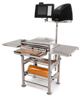 A stainless steel food packaging machine with a touchscreen control panel, impressive roll film capacity, and heated seal plate for sealing trays or containers, set against a plain white background. Orange plastic film sits on the holder above the rectangular sealing area.