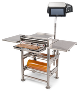 A commercial stainless steel wrapping machine with a mounted touchscreen, roll film capacity, side shelves, heated seal plate, and cutting tray. The device stands on four legs and is designed for efficient packaging of food or products.