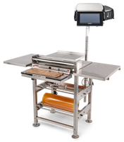 A commercial stainless steel wrapping machine with a mounted touchscreen, roll film capacity, side shelves, heated seal plate, and cutting tray. The device stands on four legs and is designed for efficient packaging of food or products.