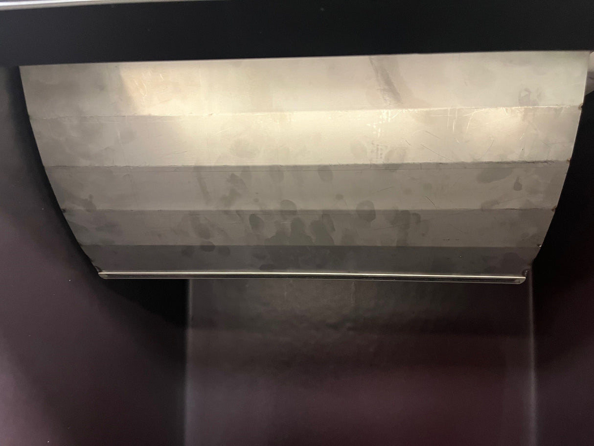 Close-up of the inside of an upright bin, showing a curved, brushed metal bin deflector partially open at the top. The deflector has visible smudges and fingerprints. The bin’s interior sides are dark and smooth with a horizontal metal rod below.