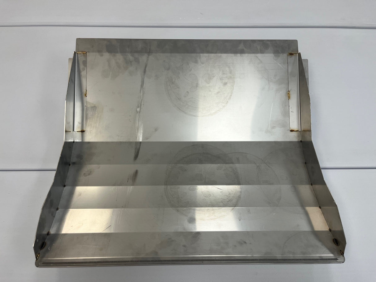 A rectangular metal sheet with three angled bends forms a stepped surface, resembling a bin deflector used in Icetro America upright bins. Two vertical side flanges show visible spot welds. The brushed, slightly reflective finish displays surface marks and circular patterns.