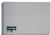A stainless steel modular cube ice maker by Ice-O-Matic, featuring a rectangular design with half-size cube production. Two small blue and red certification stickers and a prominent Ice-O-Matic logo are visible on the lower left corner.