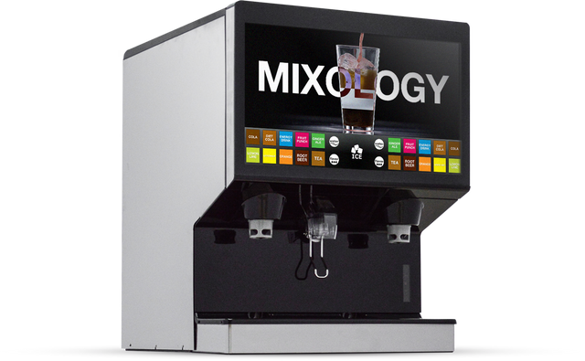 A modern countertop beverage dispenser with a touchscreen displaying MIXOLOGY, an image of a fizzy drink, and colorful drink icons. Below the screen are two dispensers, an ice chute, and a drip tray. The machine is sleek in silver and black.