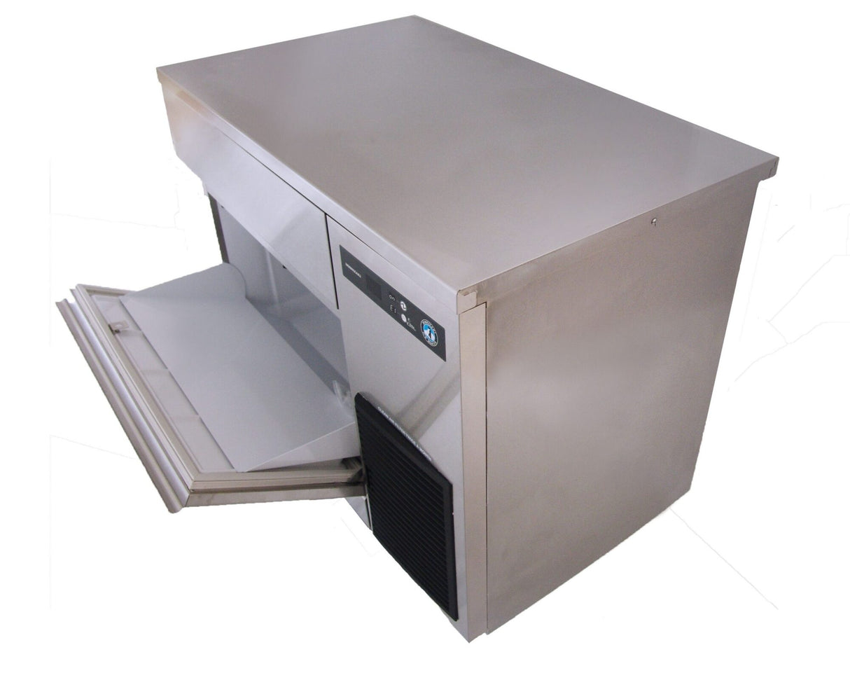 A Hoshizaki undercounter ice maker with a front panel open, showcasing the ice storage compartment. The stainless steel, cube-style ice maker features a flat top, control buttons, and a vent on the side, set against a white background.