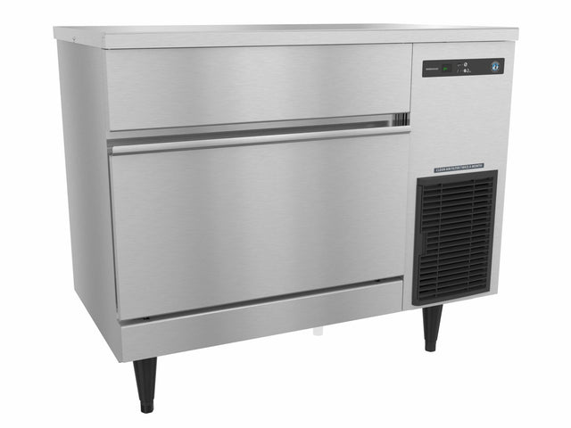 A commercial Hoshizaki stainless steel ice storage bin with black adjustable legs, a horizontal handle, and a digital control panel on the upper right. This undercounter ice maker features a smooth, reflective surface and a vent below the control panel.