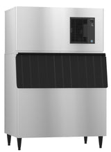 A large commercial Hoshizaki cube-style ice maker with a black front panel and ventilation grill on the upper right side. The machine has four short black legs and a rectangular, industrial design ideal for restaurants or commercial kitchens.