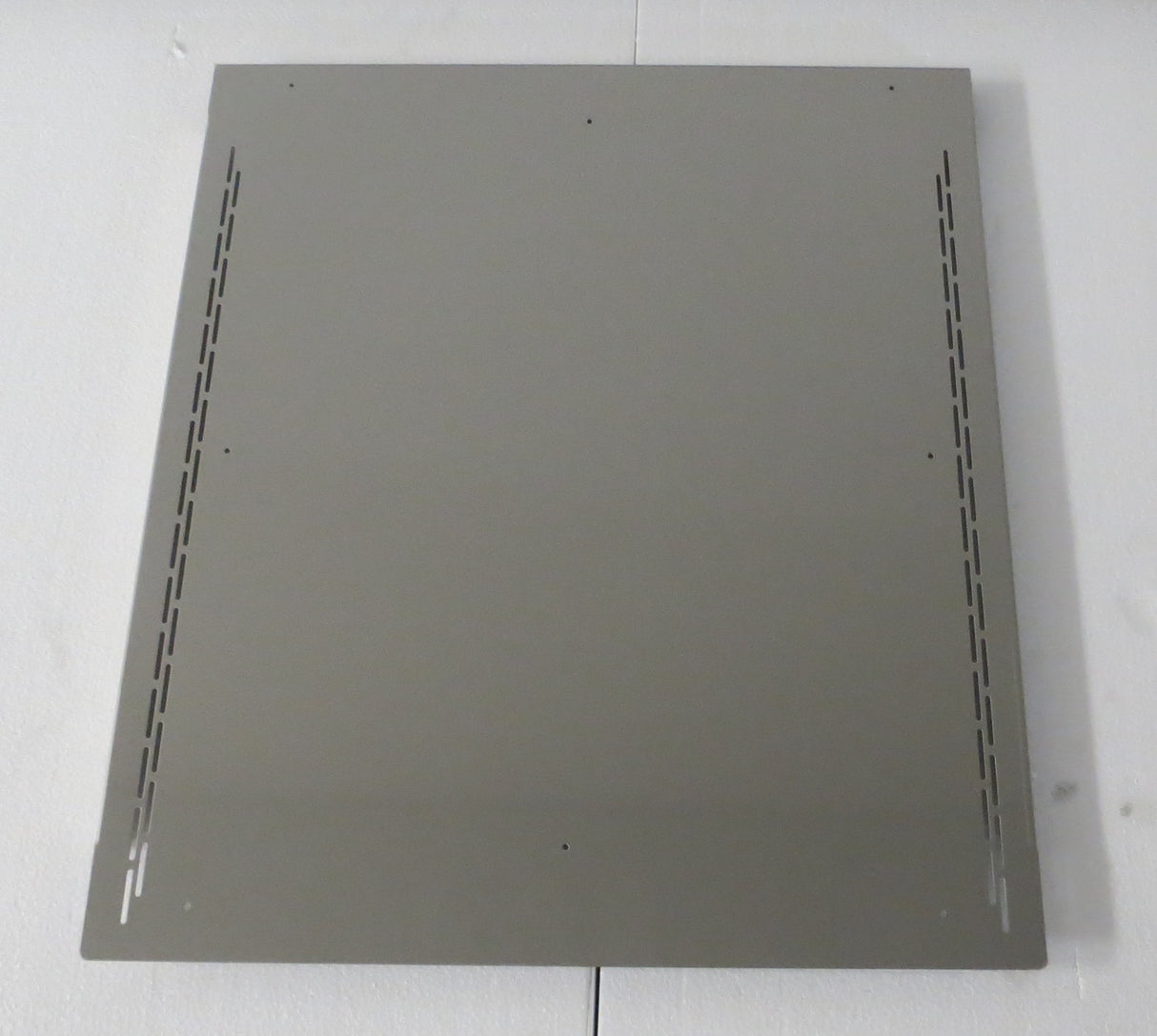 A rectangular metal sheet with a matte gray finish, featuring four small holes near each corner and two rows of elongated ventilation slits along the left and right edges, serves as a bin adapter for a 30" head on 48" bin from Icetro America.