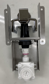 A metal wall-mounted bracket holds an Icetro America chrome and black dispenser above a white plastic valve assembly with a pink ring, set against a plain surface. The components are aligned vertically and securely attached to the bracket.