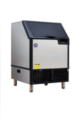 A commercial cube-style ice maker with a stainless steel exterior, black lid, front vents, warning labels, and the brand name ICETRO faintly visible on the front. The machine stands on four metal legs and boasts a modern, industrial design.