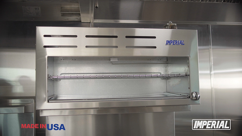 A 304 stainless steel Pro Series Cheese Melter commercial broiler oven with an infra-red burner and metal rack is mounted on a kitchen wall. The oven features vent slots and a blue IMPERIAL logo, with MADE IN USA and IMPERIAL branding in the corners.