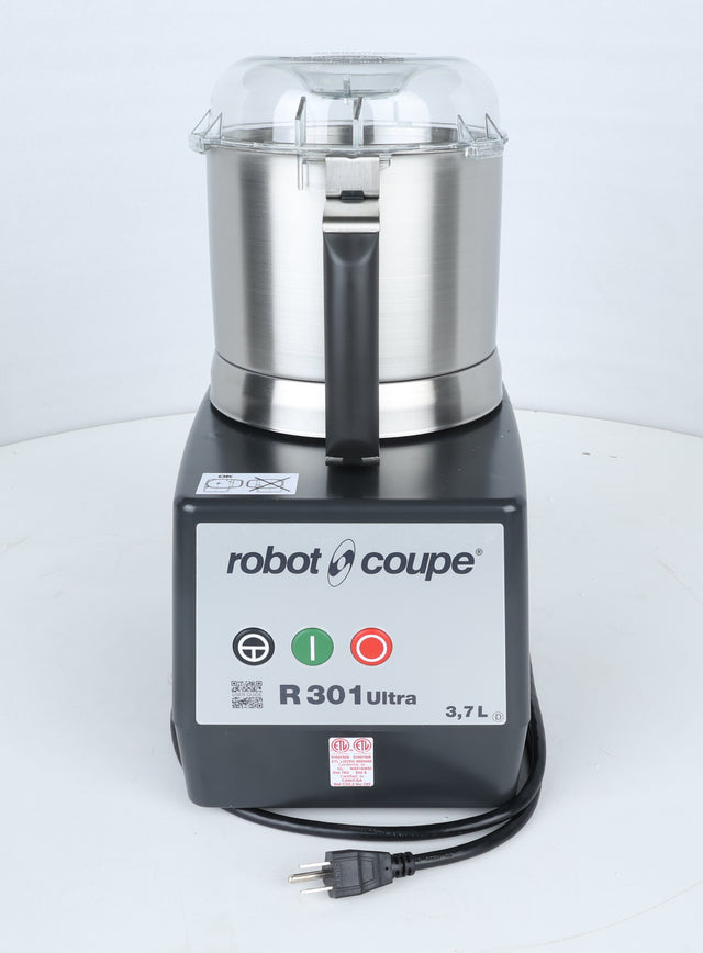 A Robot Coupe R301U.D commercial food processor is shown upright on a white surface. The stainless steel bowl has a clear lid, ideal for efficient vegetable prep in busy kitchens. The control panel displays green and red power buttons, model information, and a 3.7-liter capacity. The power cord with plug is visible.