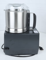 A stainless steel commercial food processor, the Robot Coupe R301U.D, with a black plastic base, clear plastic lid, and black handle sits on a white surface. Perfect for efficient vegetable prep tasks, an electric cord with a plug is wrapped around the base. A caution sticker is visible on the top right corner of the base.