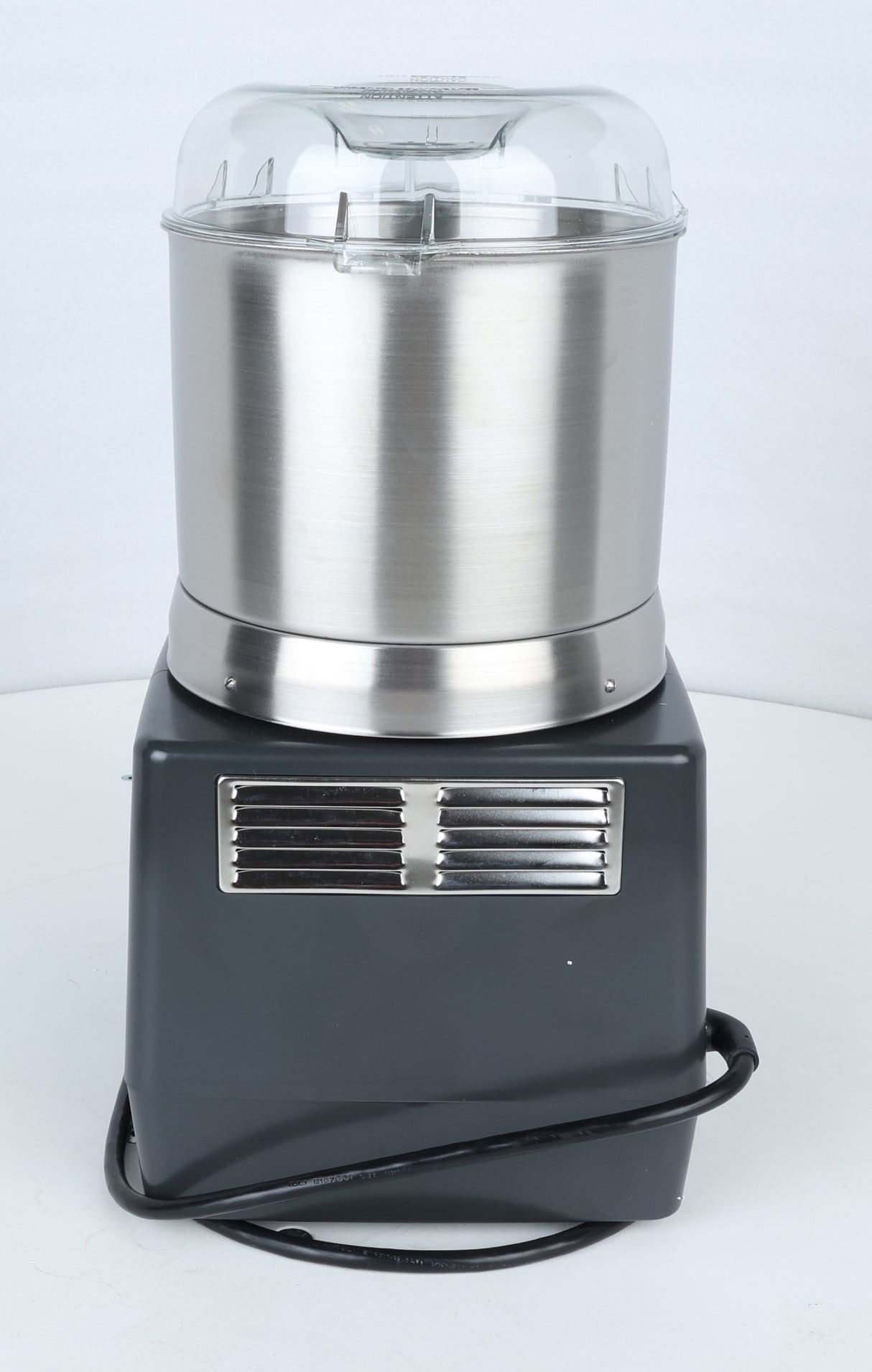 A stainless steel and black countertop ice cream maker with a clear plastic lid sits on a white surface; a ventilation grill and a coiled black power cord are visible at the base, echoing the sleek, functional design found in commercial food processor models like the Robot Coupe R301U.D.