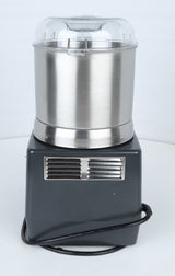 A stainless steel and black countertop ice cream maker with a clear plastic lid sits on a white surface; a ventilation grill and a coiled black power cord are visible at the base, echoing the sleek, functional design found in commercial food processor models like the Robot Coupe R301U.D.