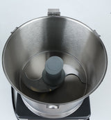 A top-down view of an empty stainless steel commercial food processor bowl with a sharp metal S-blade attachment in the center, set on a black base against a white background. The bowl, compatible with a Robot Coupe food processor, features a brushed metal texture and two side handles.