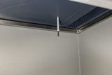 A close-up of a metal room corner shows a ceiling-mounted, thin white temperature sensor using thermistor technology, extending downward amid smooth stainless steel walls and a dark, slightly textured ceiling.