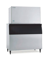 A stackable commercial ice maker with a silver body and large, rectangular shape. The top cube-style section makes ice, while the lower storage bin features a black, slanted front door. The unit stands on four sturdy black legs.
