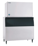 A large Hoshizaki Ice Maker with a white upper section and black front lower bin stands on four legs. The top section features a small round blue and white sticker. Its utilitarian, industrial design is ideal for making crescent cube ice in restaurants or cafeterias.