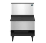 A commercial Hoshizaki stainless steel ice maker with a black louvered vent at the bottom, black slanted front panel, and short black legs. The unit features a blue and white circular logo in the upper right corner and produces cube-style ice.