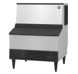 The Hoshizaki KM-301BAJ is a commercial stainless steel ice maker with a black front vent and lid, standing on four short legs. Its rectangular design efficiently produces crescent style cube ice for food service environments.