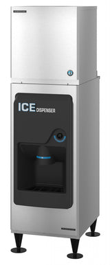 A tall, stainless steel Ice Maker stands on four black legs. The front panel features a black dispenser area with a chute, cup sensor, and the words ICE DISPENSER in bold white and blue letters. The top section is a large Cube-Style ice storage bin.