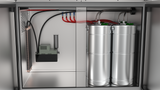 Inside a metal cabinet, two silver cylindrical tanks sit upright on the right, connected by red and black cables to a control box—part of the Krowne Mini Chill System. Above, tubing and wiring suggest a beverage or gas dispensing setup.
