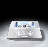 A stainless steel bar glass rinser with a square design, sloped front, and central spray nozzle—ideal for any setup using a countertop glass chiller—features the KROWNE name and crown logo on its front. It sits on a dark, textured surface against a black background.