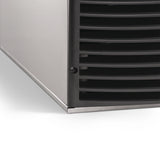 Close-up of the bottom front corner of a Scotsman stainless steel appliance with a black vented grill; a small screw is visible on the black section, and the unit with Undercounter Floor Mount Kit rests on a white surface beneath ADA countertops.