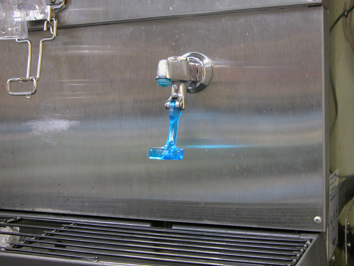 A Scotsman metal beverage dispenser with a spigot is dispensing a stream of bright blue liquid. The liquid drips toward a black grate below, with blue residue visible on the spigot and nearby surfaces. Ideal for use with an ID150 water glass filler kit.