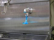 A Scotsman metal beverage dispenser with a spigot is dispensing a stream of bright blue liquid. The liquid drips toward a black grate below, with blue residue visible on the spigot and nearby surfaces. Ideal for use with an ID150 water glass filler kit.