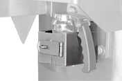Close-up of a metallic safety latch securing a transparent plastic container with a black handle to a Vulcan stainless steel machine, featuring a hinged latch locked by a metal pin. The background is mostly out of focus.