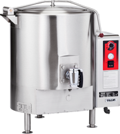 A large, stainless steel commercial tilt skillet resembling a stationary kettle, with a black handle, control panel featuring dials and switches, temperature gauge, “Vulcan” branding, four sturdy legs, and a handled lid on top.
