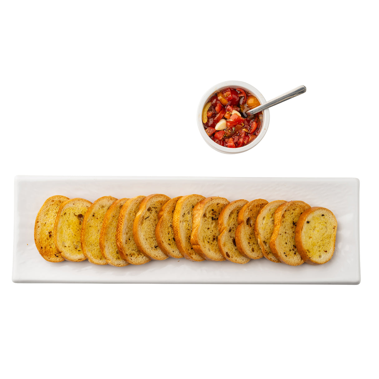 A rectangular serving dish from the Frostone Collection displays 13 slices of toasted baguette in a row, with a small white bowl of tomato bruschetta and a metal spoon above, all set against a clean white background.