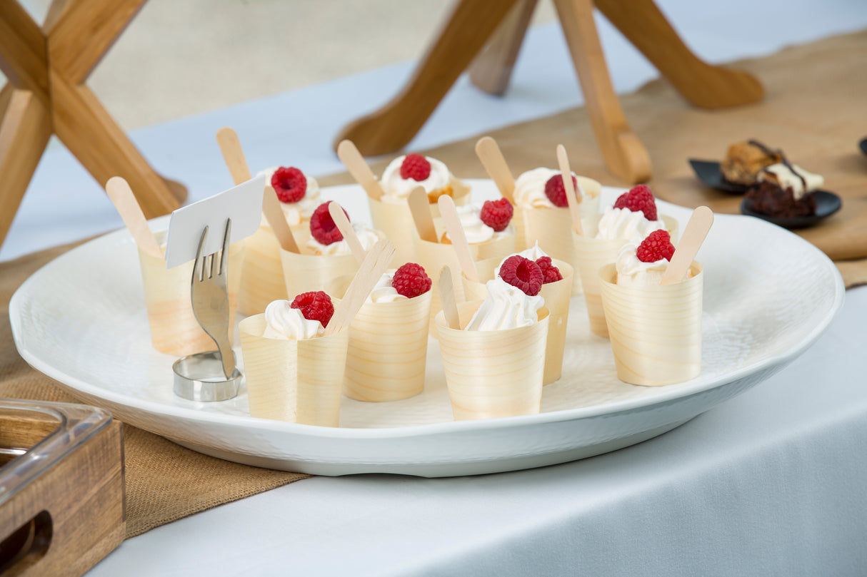 A white melamine tray from the Frostone Collection holds several small cups filled with whipped cream, each topped with fresh raspberries and a wooden spoon. A blank white card stands in a metal holder on the table covered with a white cloth.