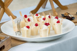 A white melamine tray from the Frostone Collection holds several small cups filled with whipped cream, each topped with fresh raspberries and a wooden spoon. A blank white card stands in a metal holder on the table covered with a white cloth.