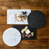 Two rectangular and two round white marble serving boards rest on a wooden table; one is topped with cheese, crackers, apple slices, walnuts, and salami, another with cheese, nuts, blackberries, and orange berries; other boards are empty.