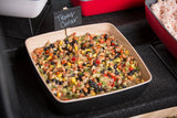 A square TableCraft Frostone Naturals melamine bowl is filled with Texas caviar—a colorful salad of black beans, black-eyed peas, corn, peppers, and onions. A chalkboard sign labeled Texas Caviar rests on the bowl atop a black textured surface.