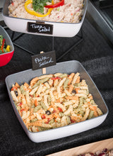 A square melamine bowl from the TableCraft Frostone Naturals collection holds tri-color rotini pasta salad with olives and diced vegetables. A small black sign labeled Pasta Salad is placed in the bowl, with Tuna Salad behind it.