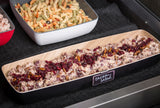 A rectangular wooden tray labeled chicken salad contains a creamy chicken mixture topped with dried cranberries and pecans. Behind it, a TableCraft Products melamine bowl holds tri-color rotini pasta salad, both set on a black cloth surface.