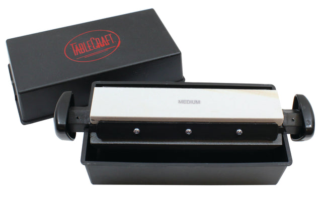 A rectangular black box with a red TableCraft logo contains a medium-grit sharpening stone set in a black holder with handles, positioned above a black tray. Part of the Three-Way Sharpener System, it offers different sharpening settings for knives.