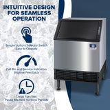 A Manitowoc ice maker with a black lid and stainless steel body sits atop a bed of ice cubes. Blue icons and text highlight features: simple selector switch, full bin/service indicators, and a delay function. This air-cooled ice machine is perfect for busy spaces.
