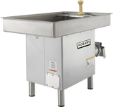 A Hobart Meat Grinder with a 3 HP motor, stainless steel pan, rectangular tray on top, beige handle, and sturdy metal legs. The side-mounted grinding mechanism and multiple warning labels enhance safety and performance.