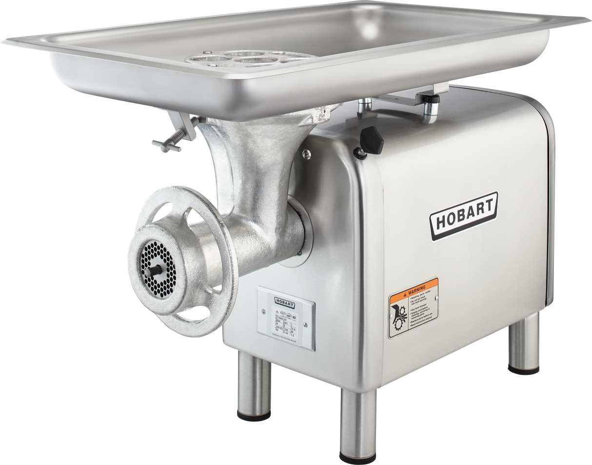 A silver Hobart Meat Chopper with a 1-1/2 HP motor features a large rectangular tray on top, metal grinding parts in front, a side-mounted handle, and warning labels. This bench type machine stands on four sturdy legs.