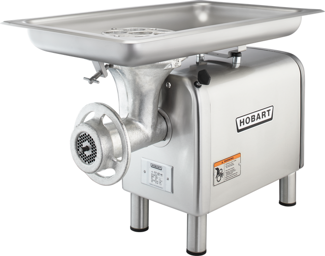 A silver Hobart Meat Chopper with a 1-1/2 HP motor features a large rectangular tray on top, metal grinding parts in front, a side-mounted handle, and warning labels. This bench type machine stands on four sturdy legs.