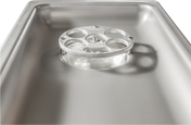 A close-up view of a shiny stainless steel Hobart commercial kitchen sink, focusing on a metal drain cover with four circular holes. The clean surface reflects light, and the drain cover casts a shadow inside the basin.