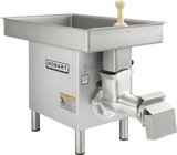 A large, industrial Hobart Meat Grinder made of stainless steel with a rectangular tray on top, a cream-colored handle, metal grinding attachment, four sturdy legs, and a robust 3 HP motor for powerful performance. The Hobart logo and safety labels are visible.