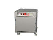 A Metro C5 6 Series stainless steel heated holding cabinet on wheels, featuring a front door, large metal handles, and a control panel with knobs and a gauge above the door, is shown against a plain white background.